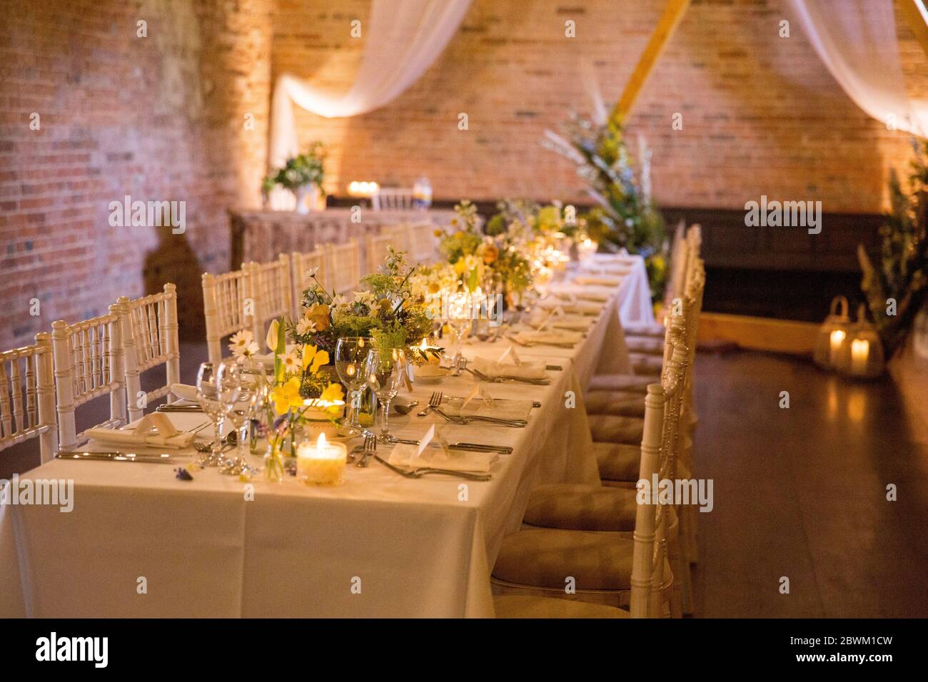 Long dining table with festive place settings for a naming ceremony in an historic barn. Stock Photo