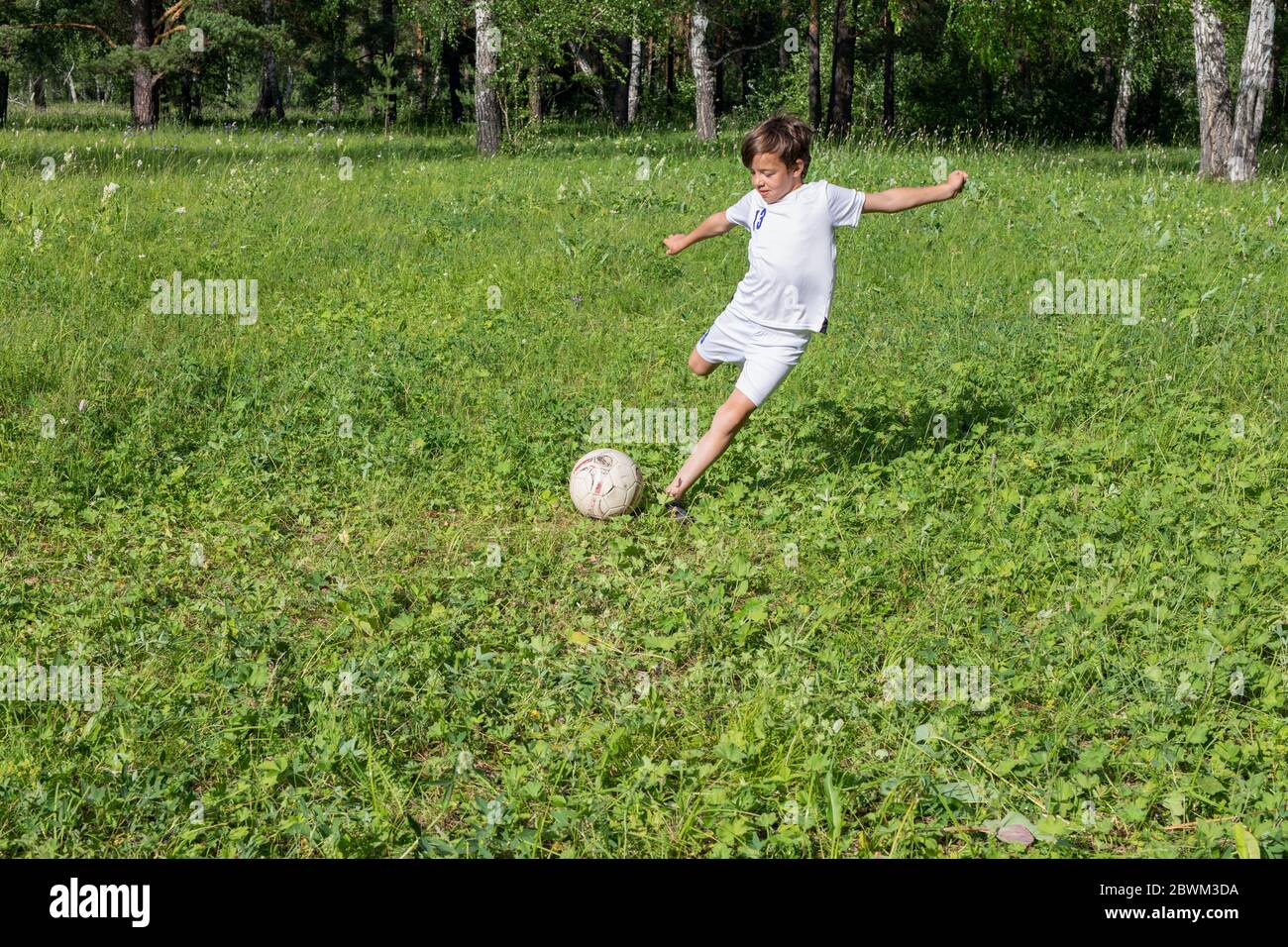 9 years old boy in white uniform playing football in green park in summer day Stock Photo