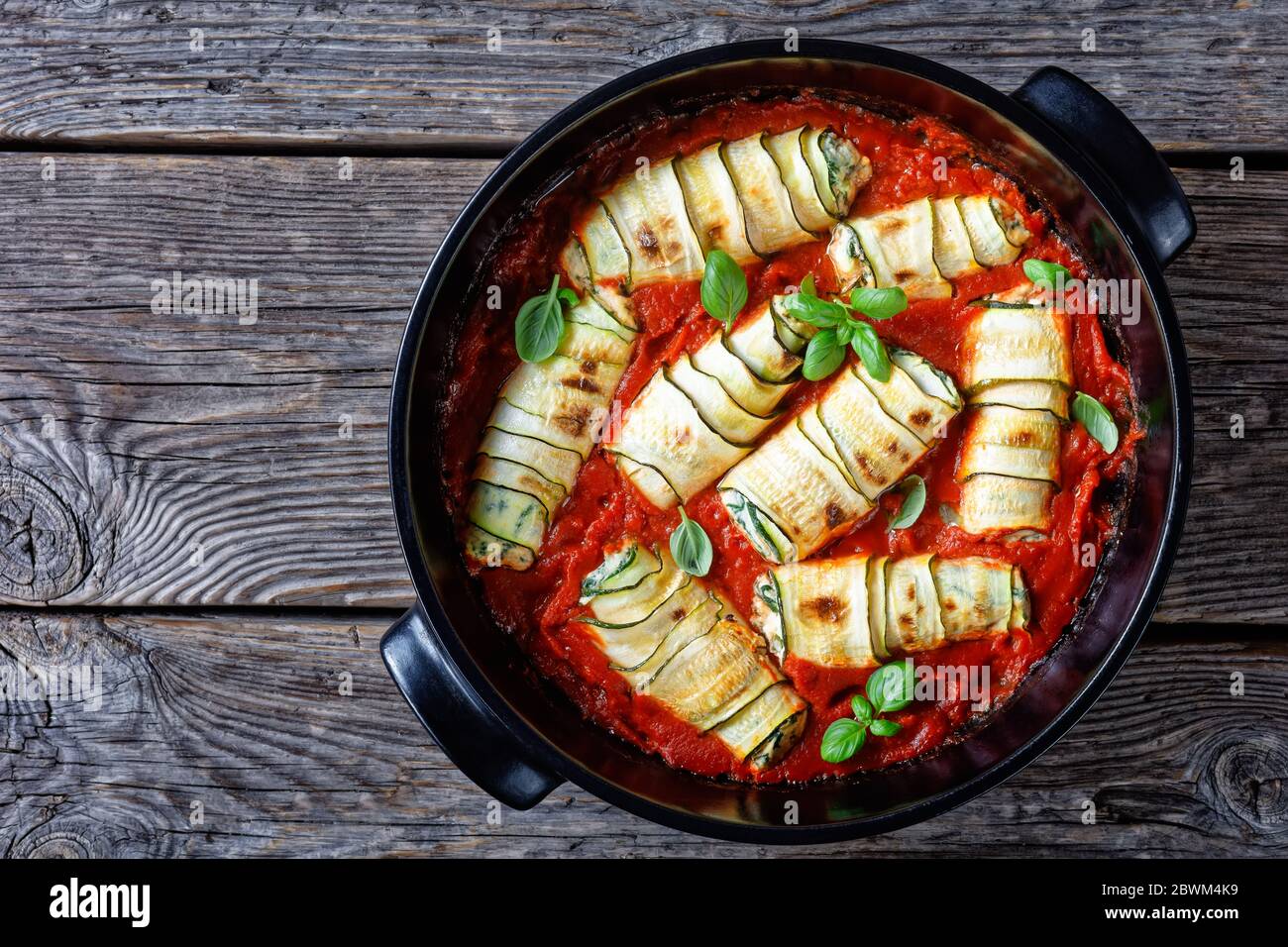 Zucchini roll-ups stuffed with fresh italian ricotta with spinach and basil leaves, garlic baked in tomato sauce, served on a black baking dish on rus Stock Photo