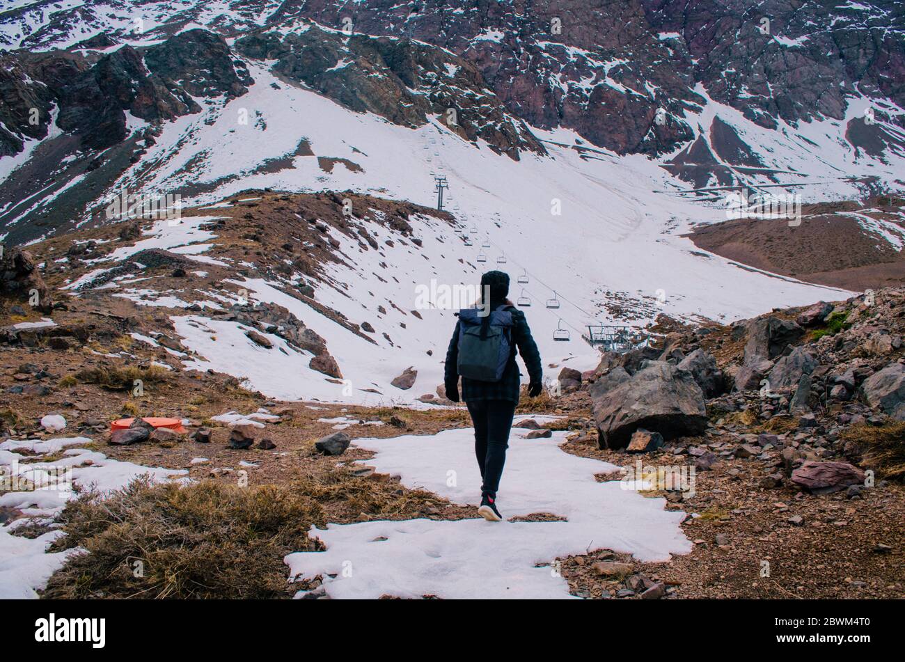 A young adult woman in black wearing a gray backpack and trekking in the Andes Mountains. Stock Photo