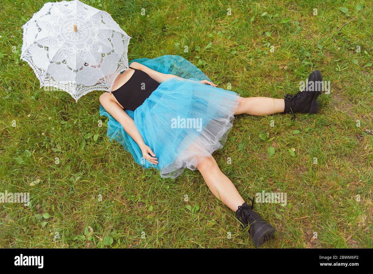 Woman in big black boots and a blue skirt lies on green grass. After party concept Stock Photo