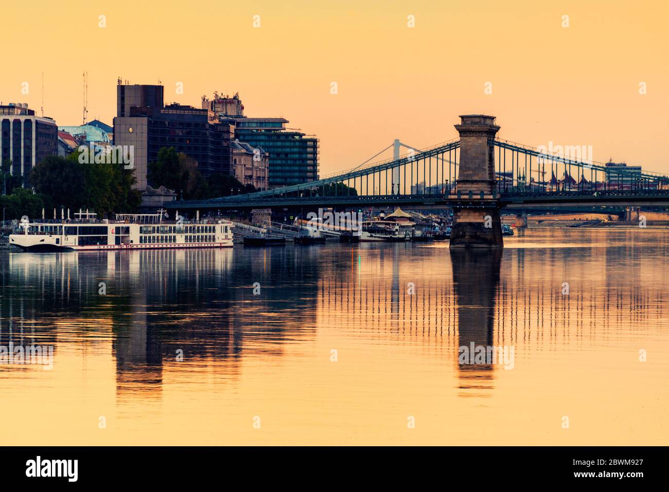 Budapest, Hungary. View of historical buildings and Chain Bridge in the morning with clear yellow sunrise sky in Budapest, Hungary. Reflection in the Stock Photo