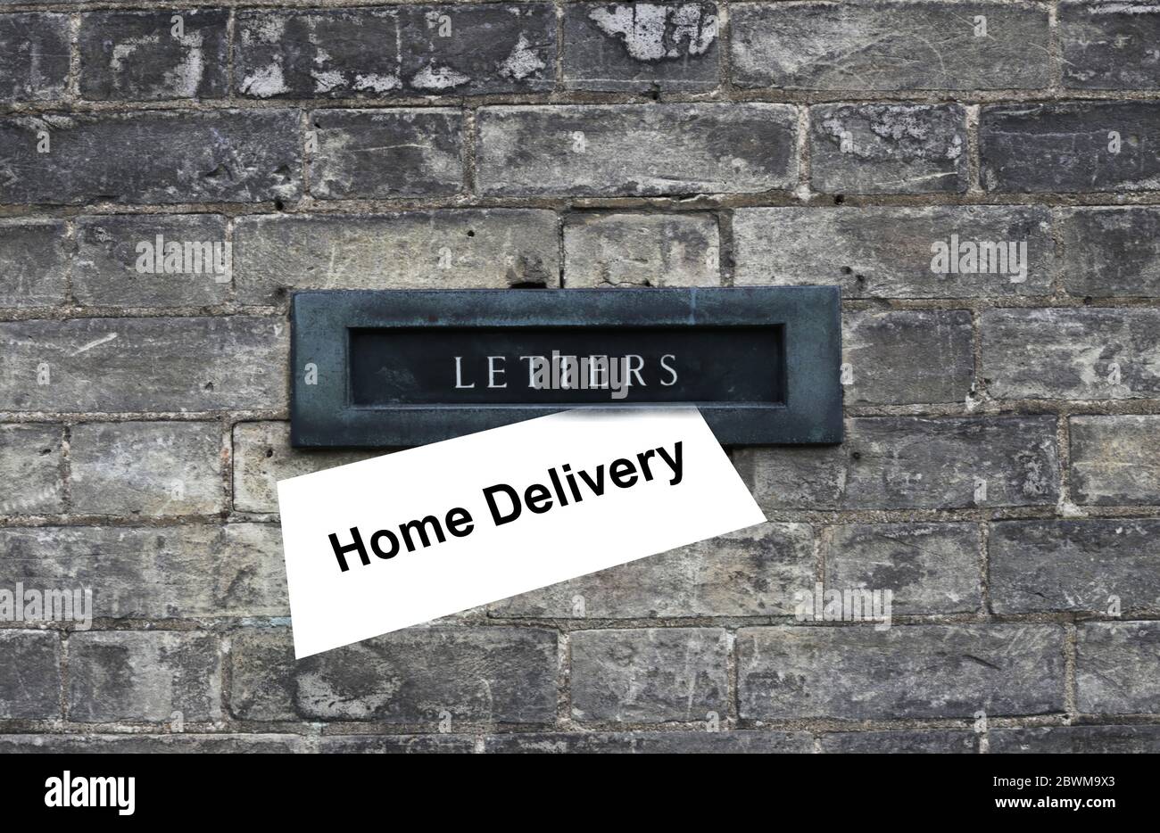 Daily magazine, letter with sign Home Delivery waiting to be picked up from the old door hole, letter box. Old brick house background. Horozontal, close up. Safety home delivery concept Stock Photo