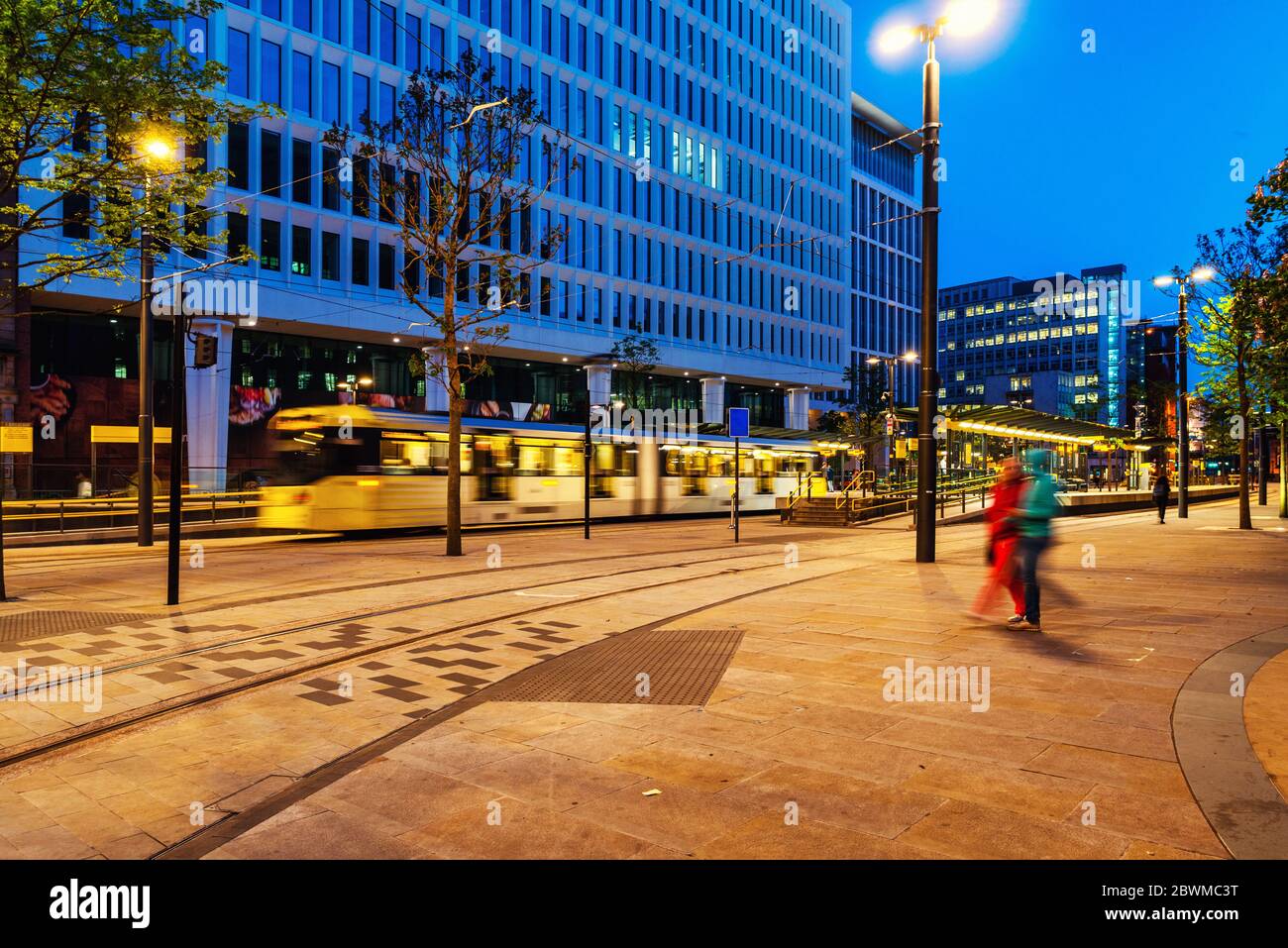 Manchester, England. Light rail yellow tram in the city center of Manchester, UK in the night. Motion blurred tram with modern buildings Stock Photo