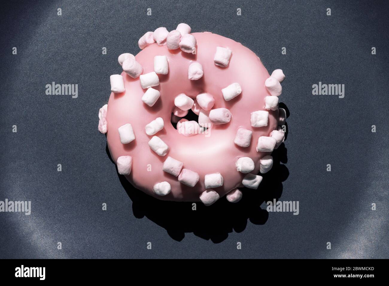 Top view of delicious single pink donat with white marshmallows on the dark grey ceramic plate. Creartive sweet food macro concept. Isolated bright Stock Photo