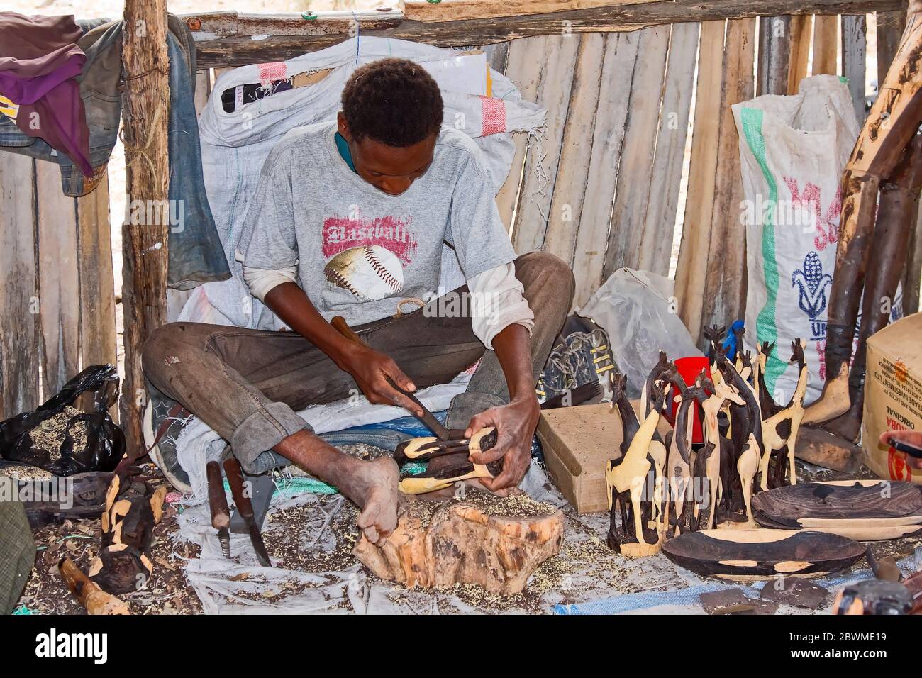 man carving ironwood; giraffe shapes; skilled artisan, working, occupation; job, animal art, sitting on ground,Tanzania; Africa Stock Photo