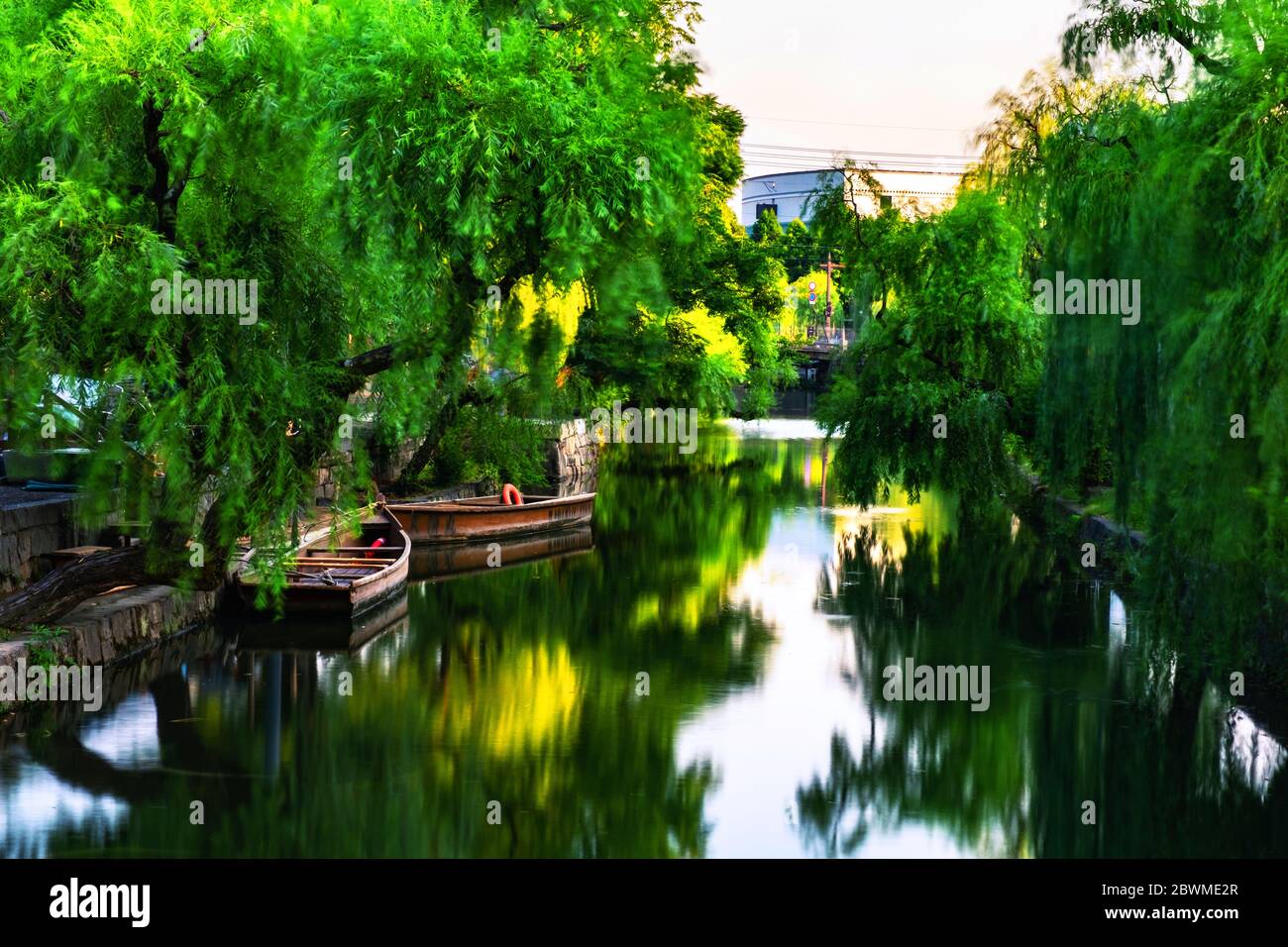 Kurashiki, Japan. View of famous canal in Kurashiki, Japan in the evening. Two old wooden boats moored, motion blurred river with green trees Stock Photo