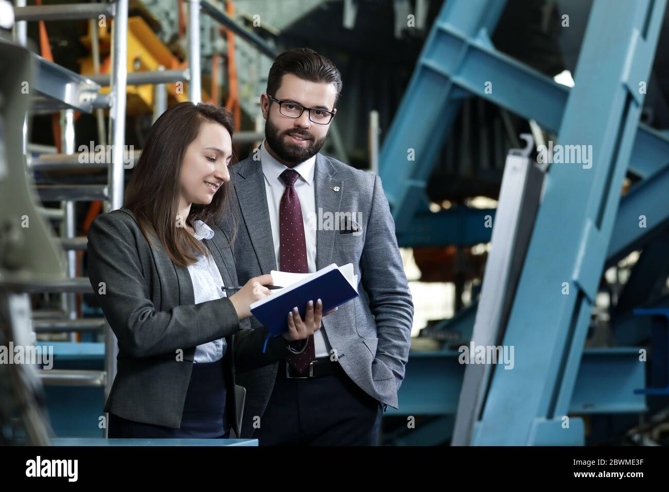 Portrait of a solid businessman with his secretary holding notebook, talking about factory financial report in a airplane manufactory. Factory manager Stock Photo