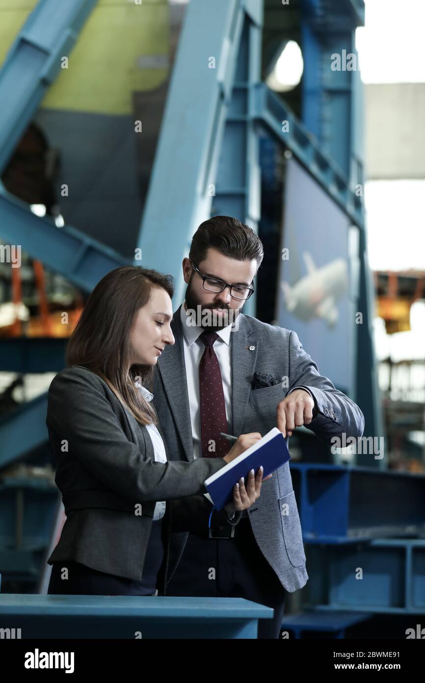 Portrait of a solid businessman with his secretary holding notebook, talking about factory financial report in a airplane manufactory. Factory manager Stock Photo