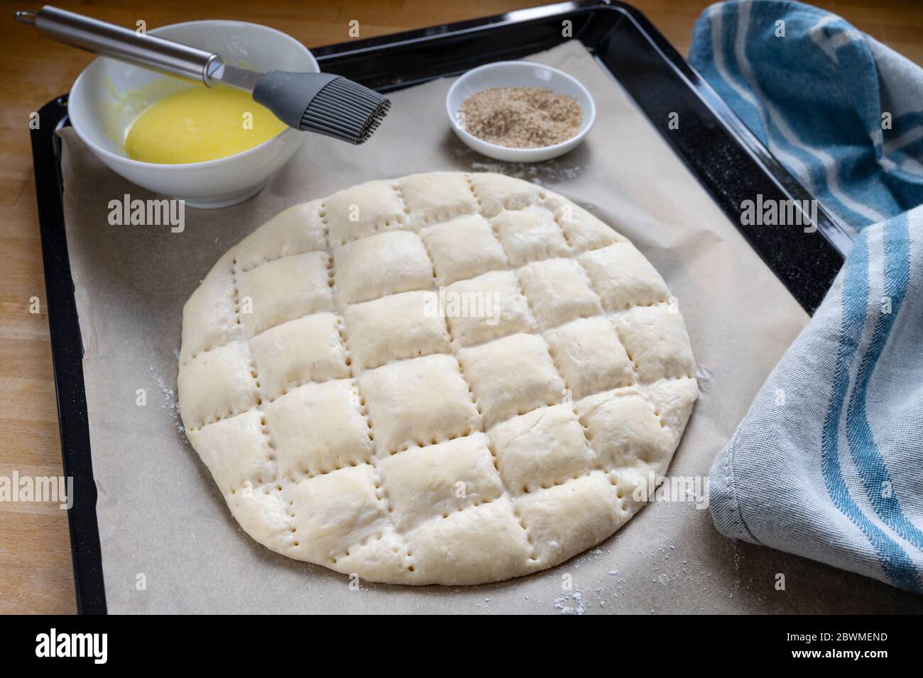 Flat bread dough with the typical pattern for Turkish Ramadan pide on a baking tray with paper, egg yolk for coating and sesame seed, selected focus, Stock Photo