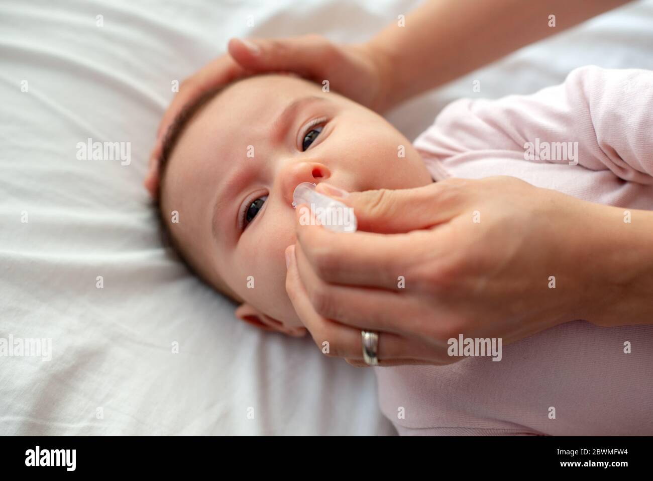 Close up of caring  mother with nasal pump to clean her baby's nose. Baby lying in bed Stock Photo