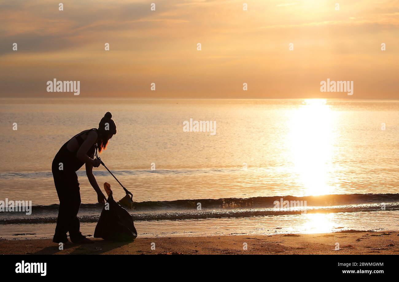 Swimmer Rebecca Kincaid picks up litter on the beach at Helen's Bay, Co. Down in Northern Ireland, as the sun comes up over the Irish Sea.  The area has seen big a rise in visitors overt he last number of days due to the warm weather.   Picture by Jonathan Porter  Credit: Jonathan Porter/Alamy Live News Stock Photo