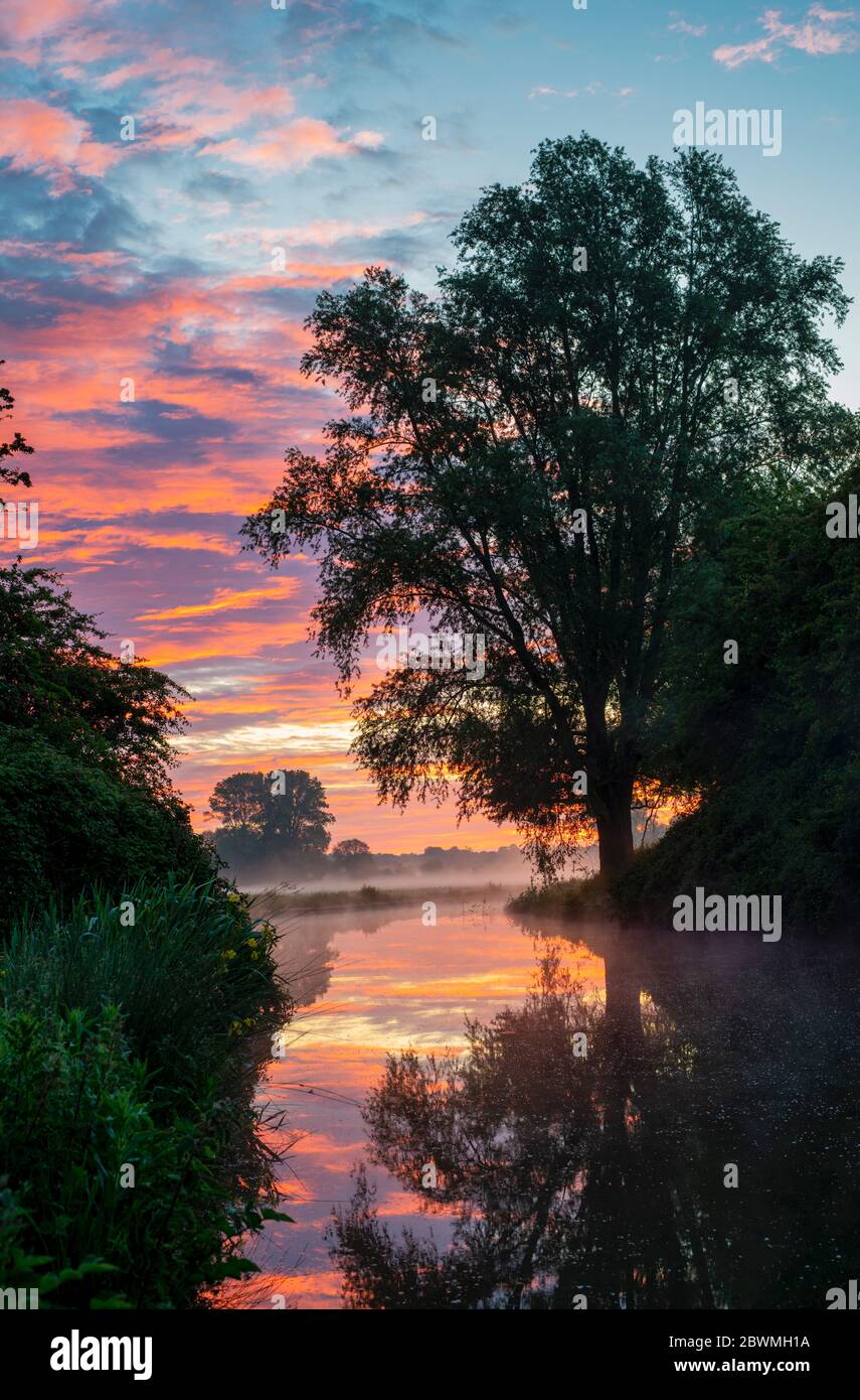Red sky and mist on the oxford canal on a spring morning just before  sunrise. Near Somerton, Oxfordshire, England Stock Photo