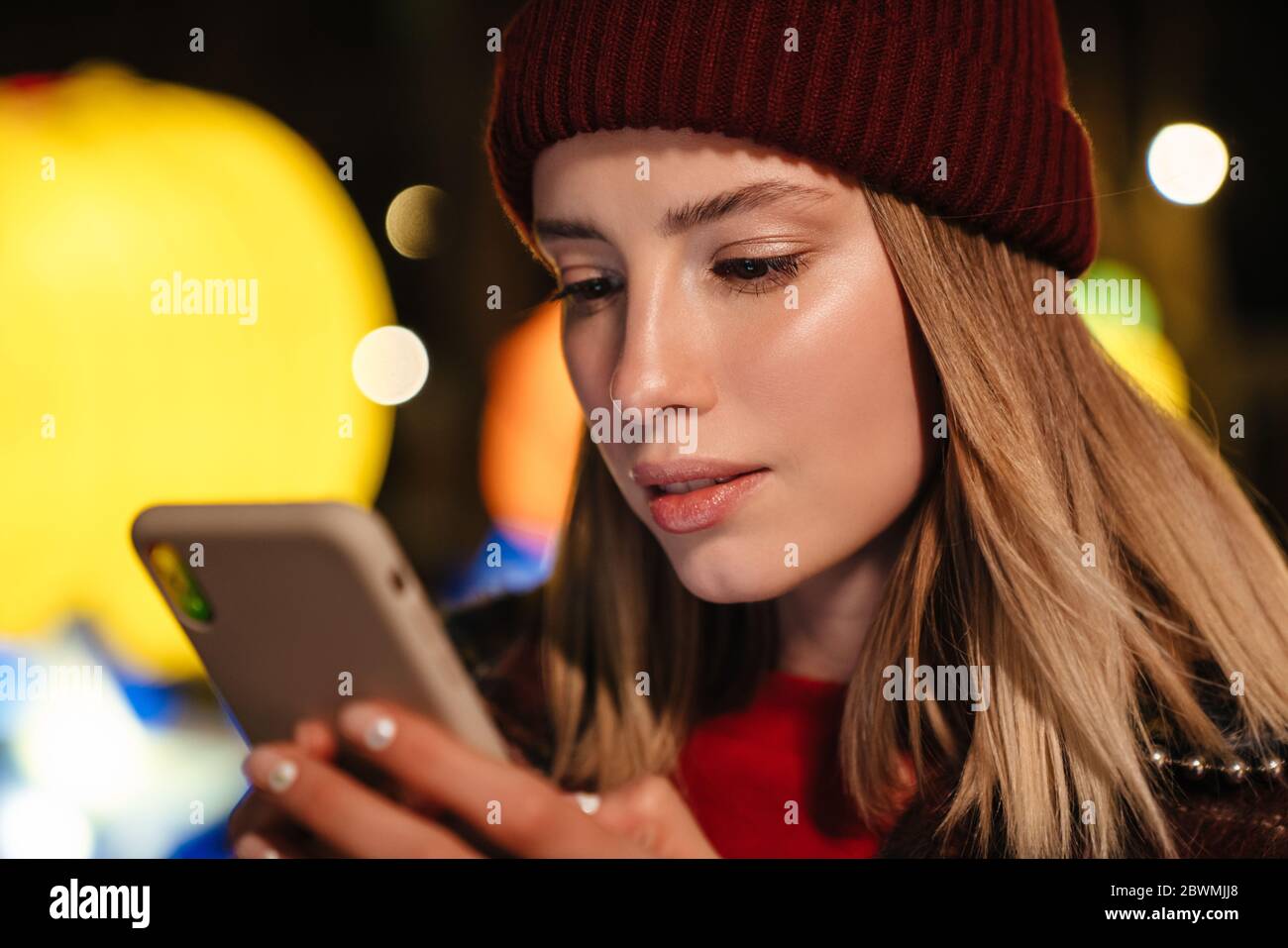 Photo of serious nice woman typing on mobile phone while walking at park with neon lighting Stock Photo