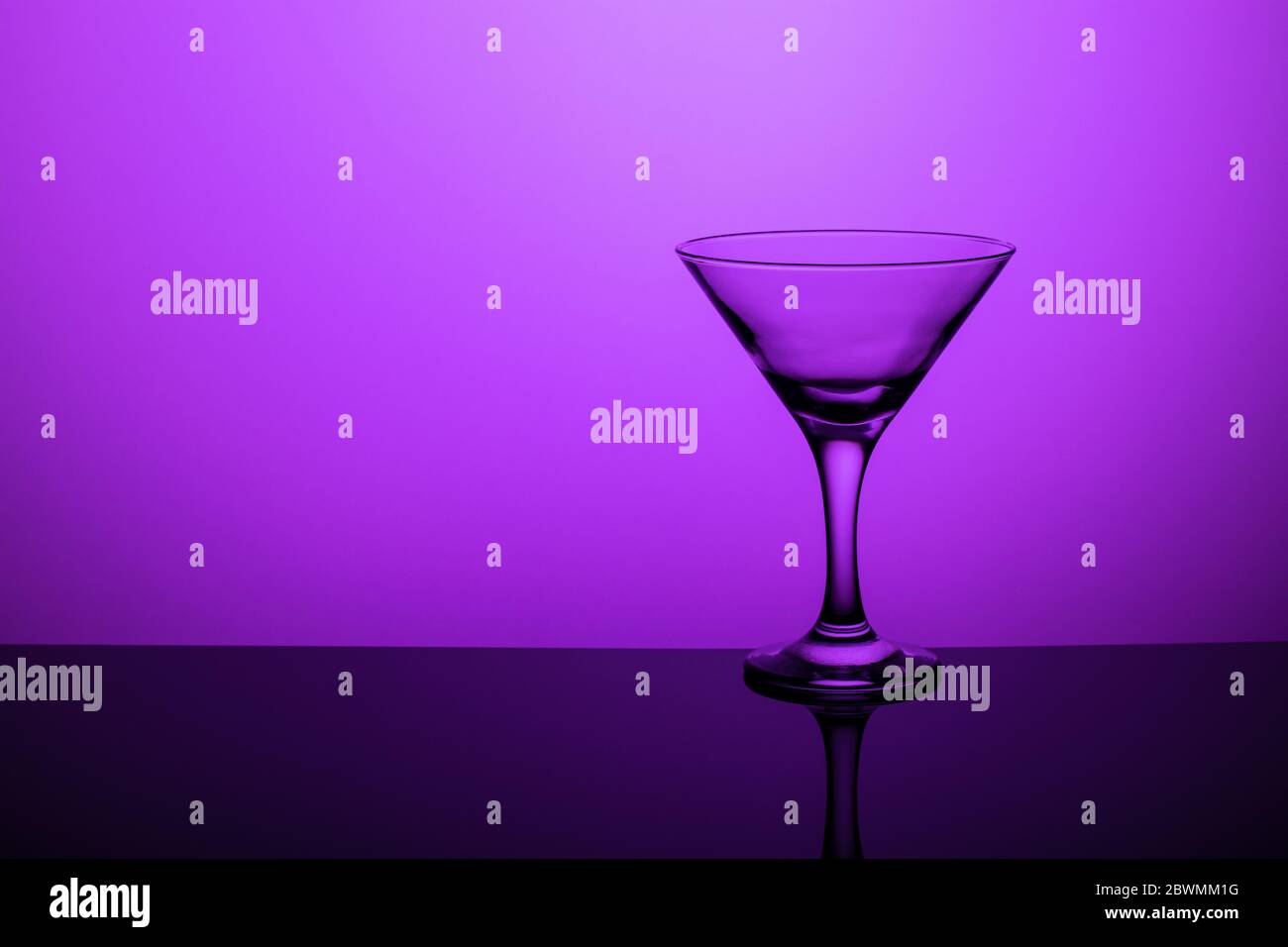 Glass goblet without wine on a thin leg stands on a mirror surface