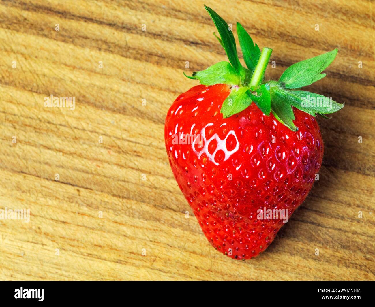 A sngle strawberry on a wooden chopping board with copy space Stock Photo