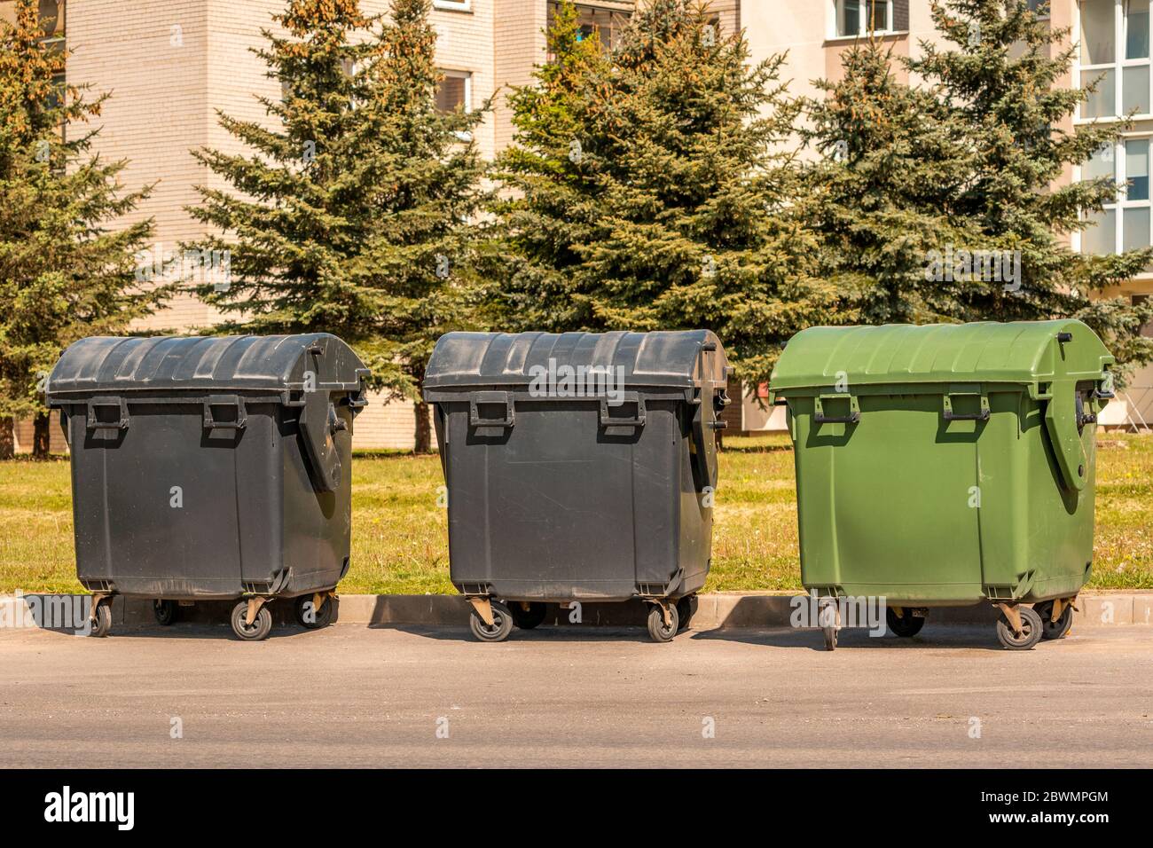 Plastic large trash cans with the lids up and garbage inside against a  brick orange wall. Big green and grey plastic dumpsters on a city street.  Waste Stock Photo - Alamy