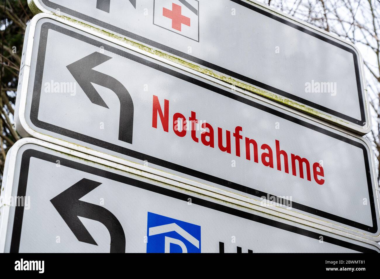 Direction sign shows the Red Cross and German text Notaufnahme, meaning emergency department, at the driveway to a large hospital Stock Photo