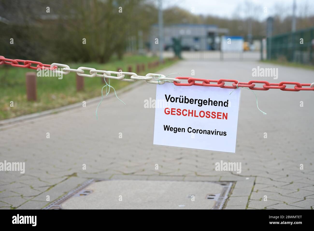 Red white chain barrier in front of a company and sign with German text Vorübergehend Geschlossen, wegen Coronavirus, meaning Temporarily Closed due t Stock Photo