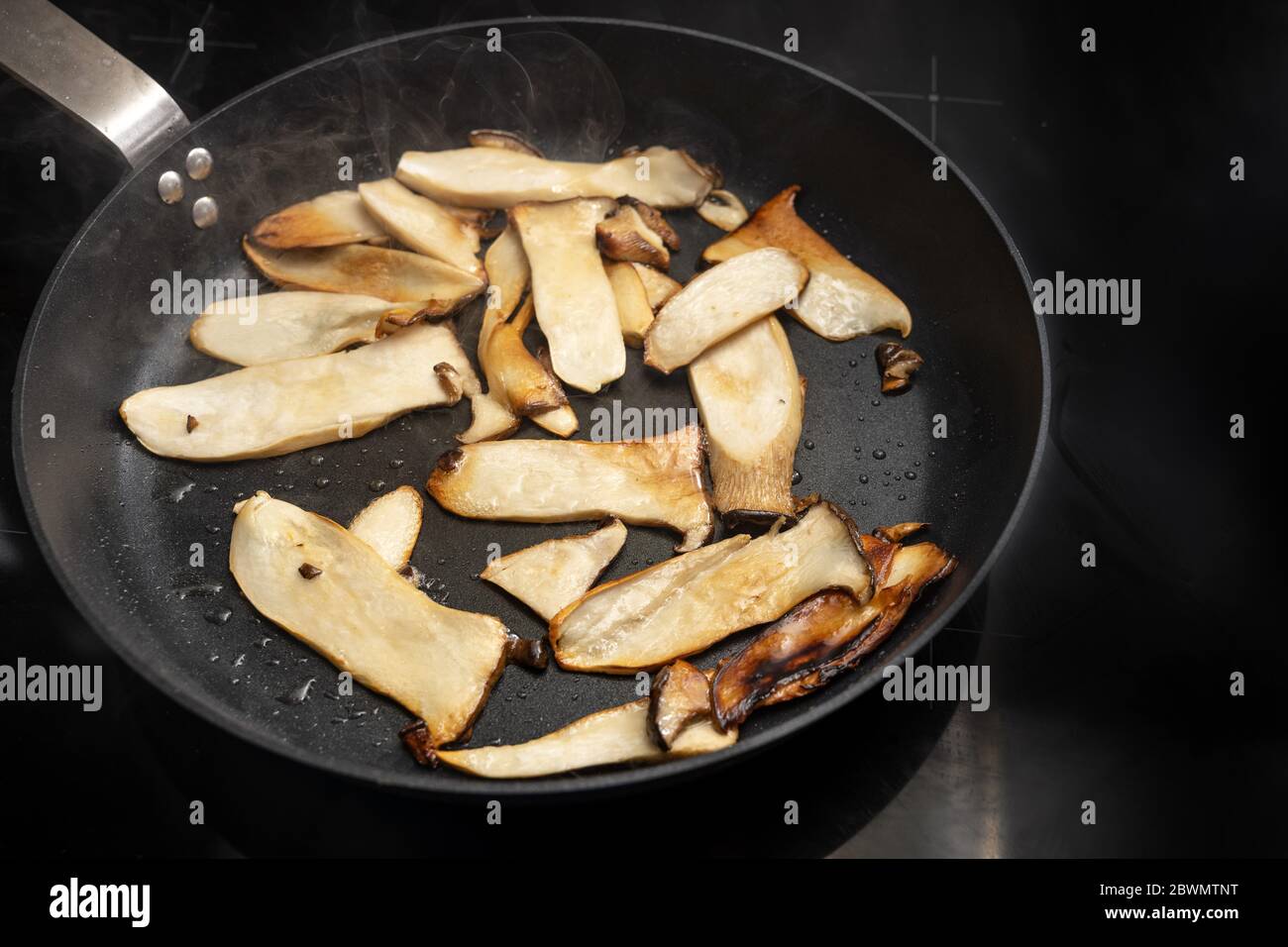 King oyster mushrooms, Pleurotus eryngii, are roasted in a black cooking pan on the stove, copy