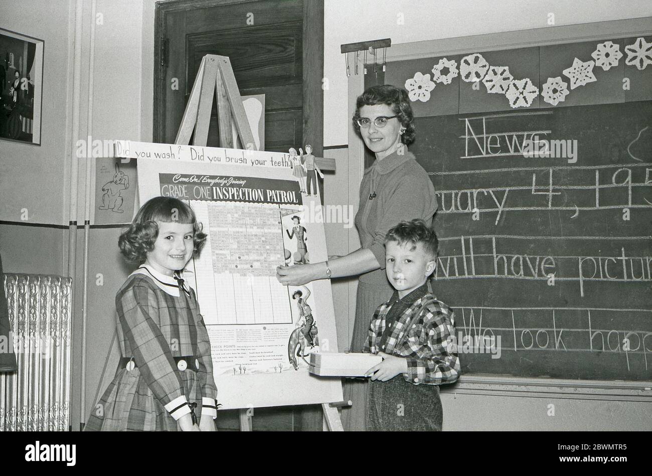 Education in the USA in the 1950s – in a classroom a teacher and two pupils are in front of a white-board with a chart concerning personal hygiene. The questions 'did you wash?' and 'did you brush your teeth?' are part of this scheme directed at grade one students in elementary school. There is hand-written news on the blackboard behind them. Stock Photo
