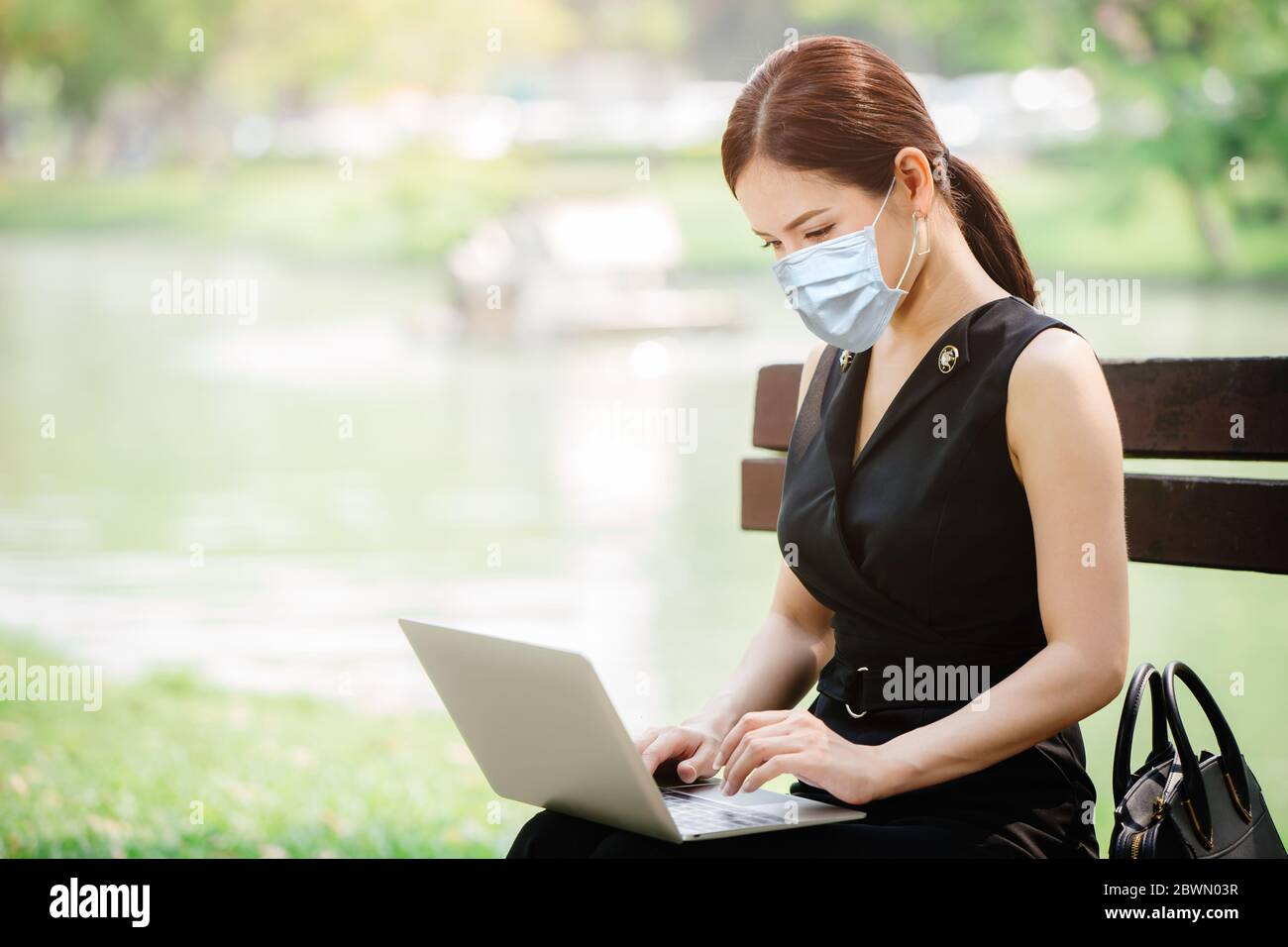 Business women online working outdoor with laptop computer and wearing face cloth mask cover for virus protection. Stock Photo