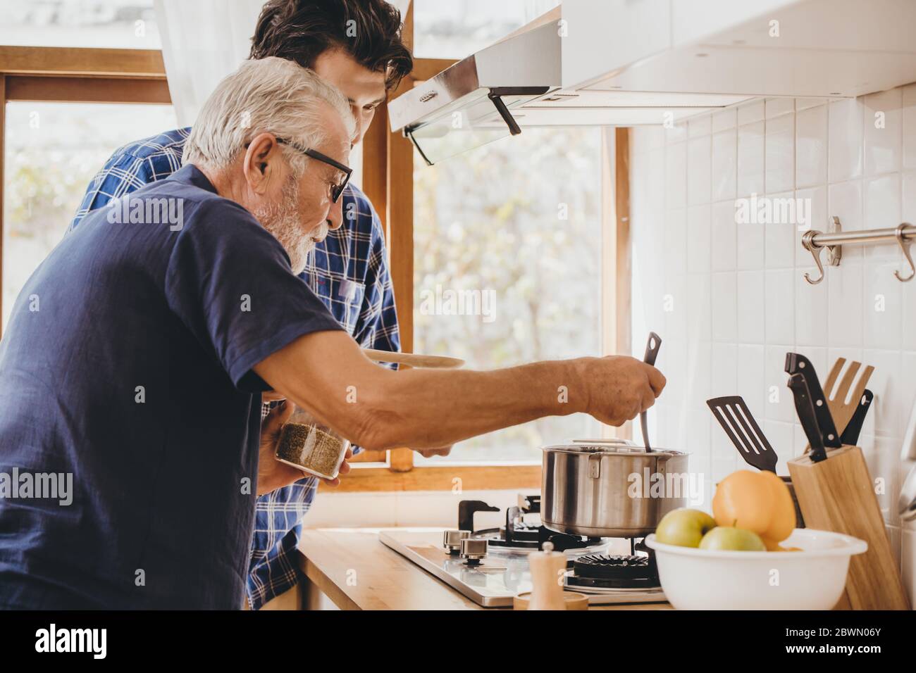 Happy senior old man enjoy teach cooking with his son at the kitchen room for stay at home leisure activity and lifestyle of people. Stock Photo