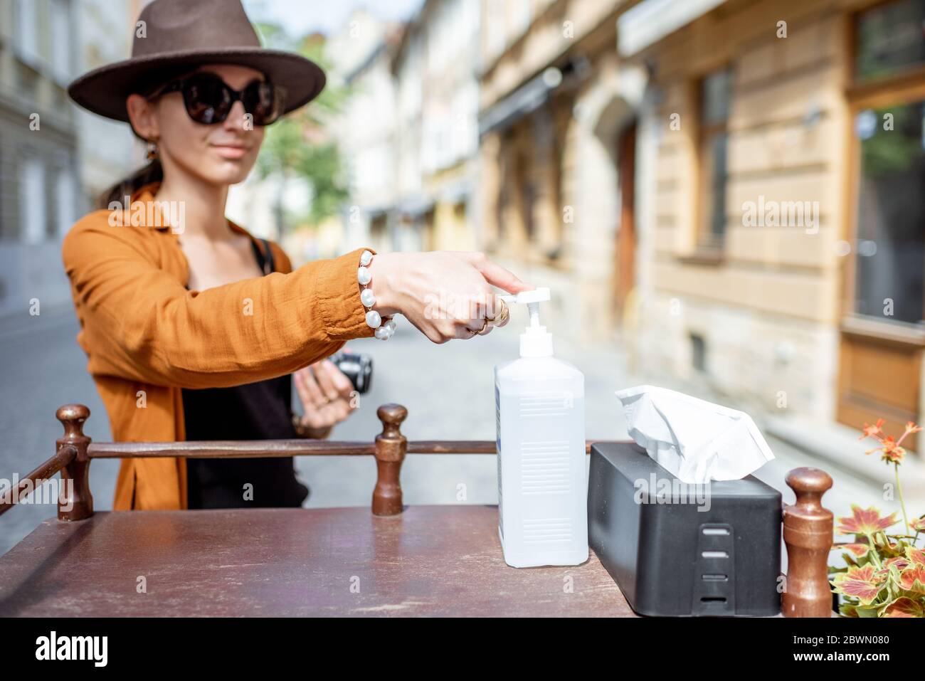 Woman disinfecting her hands, visiting cafe or restaurant outdoors. Concept of a new social rules after the epidemic Stock Photo
