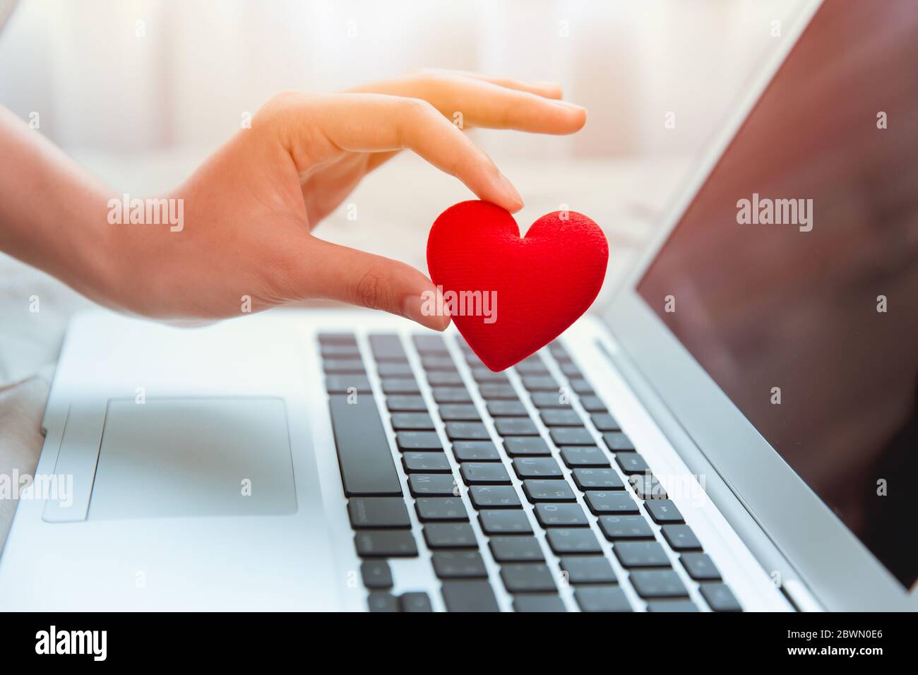 Girl hand take red heart at laptop keyboard for social online love chat and sharing encouragement over internet to fight Covid-19 virus together. Stock Photo
