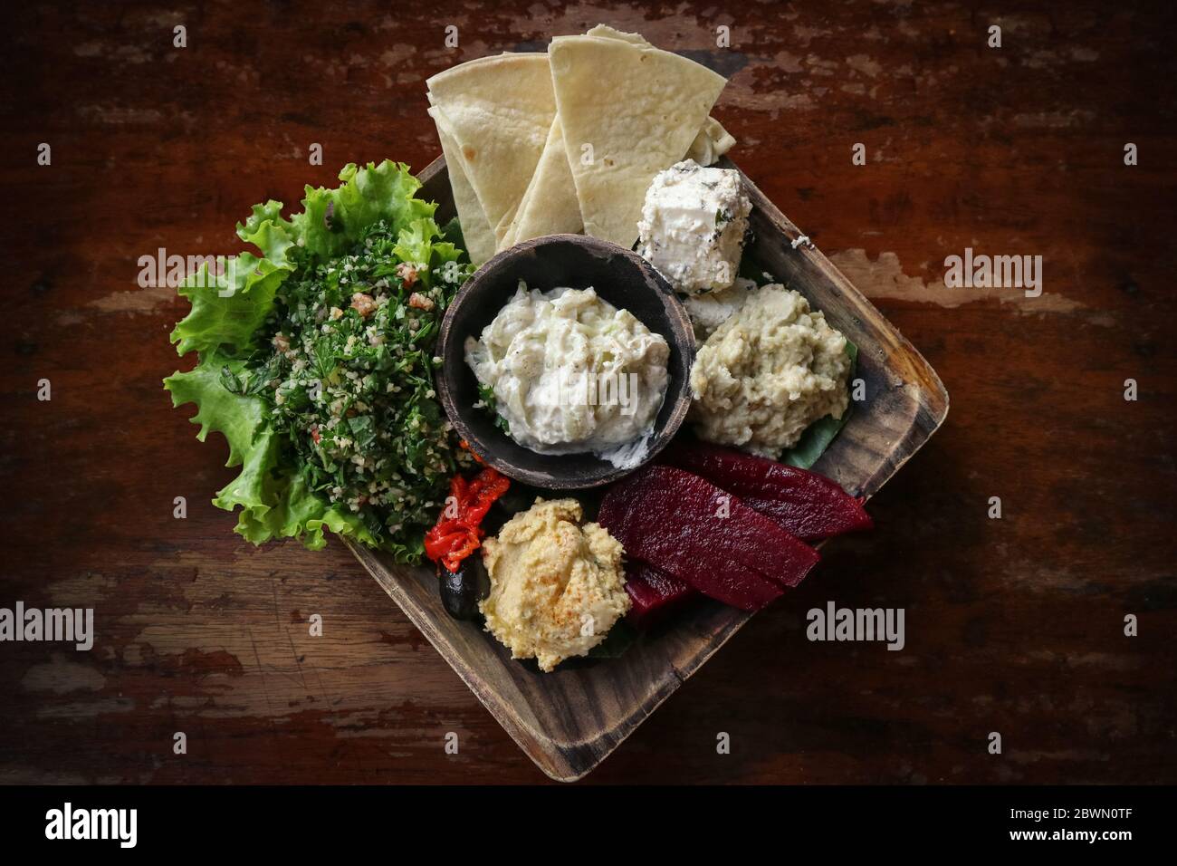 Mezze Platter with hummus, babaganoush, tabouli, roasted peppers, beet, feta cheese and kalamata olives served with pita bread on wooden background, t Stock Photo