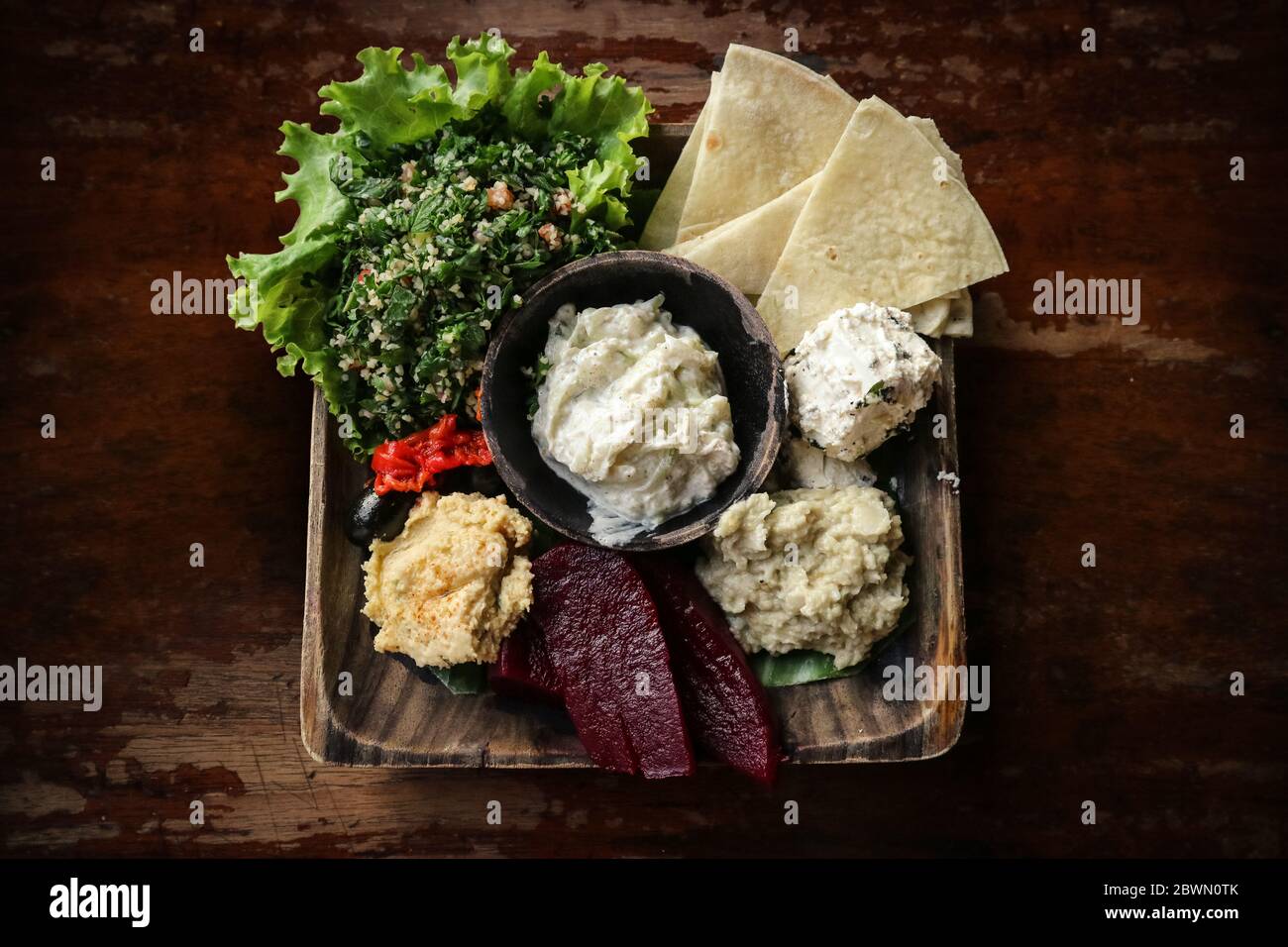 Mezze Platter with hummus, babaganoush, tabouli, roasted peppers, beet, feta cheese and kalamata olives served with pita bread on wooden background, t Stock Photo