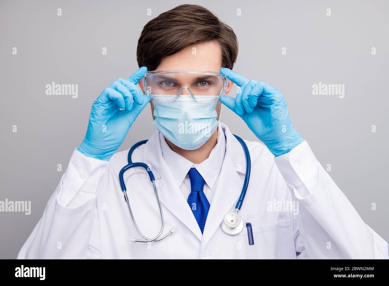 Closeup photo of attractive handsome serious doc guy professional surgeon specialist wear blue gloves facial protective mask medical uniform lab coat Stock Photo