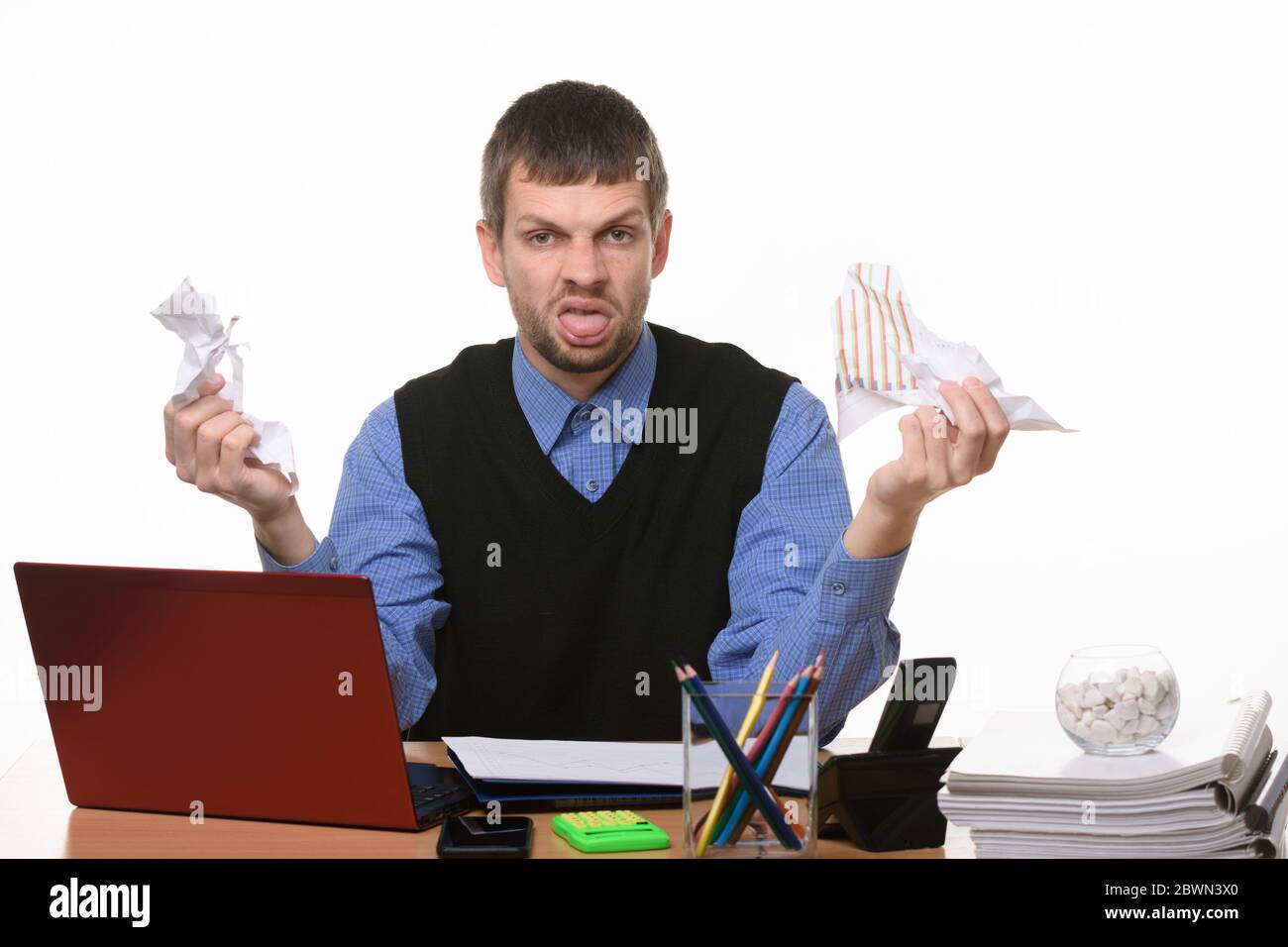 Man at work desk holds crumpled sheets of paper and shows tongue Stock Photo