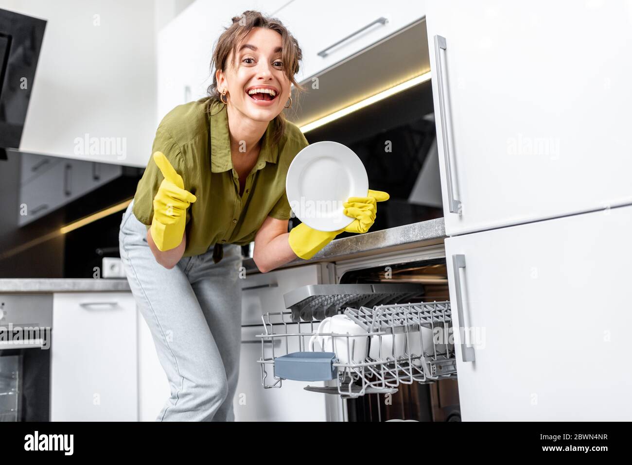 Young woman loading dishes into the dishwasher machine. Easy housework with kitchen appliances concept Stock Photo