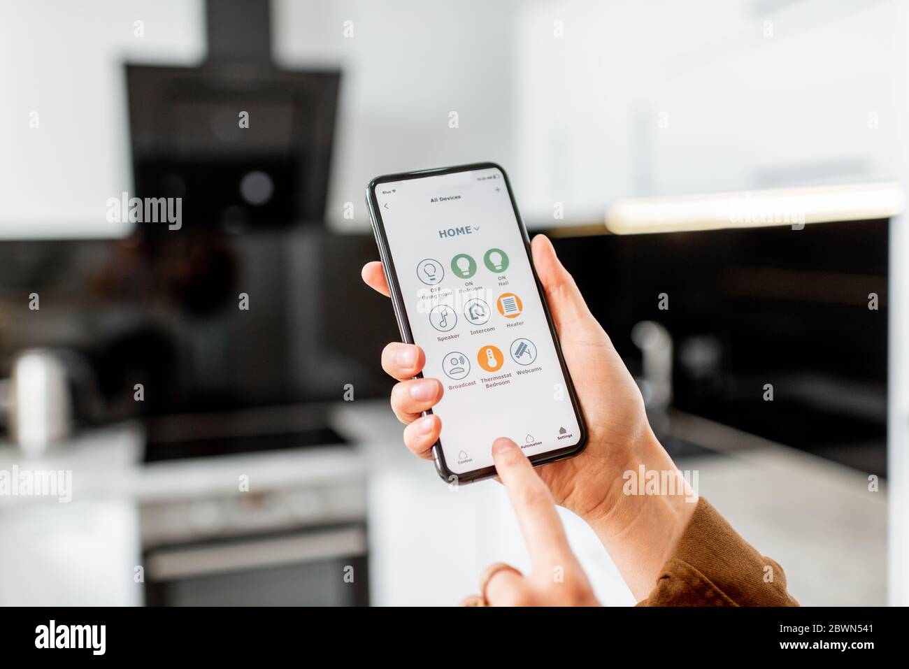 Woman controlling kitchen appliances with a smart phone, close-up on mobile device with launched smart home application. Smart home concept Stock Photo