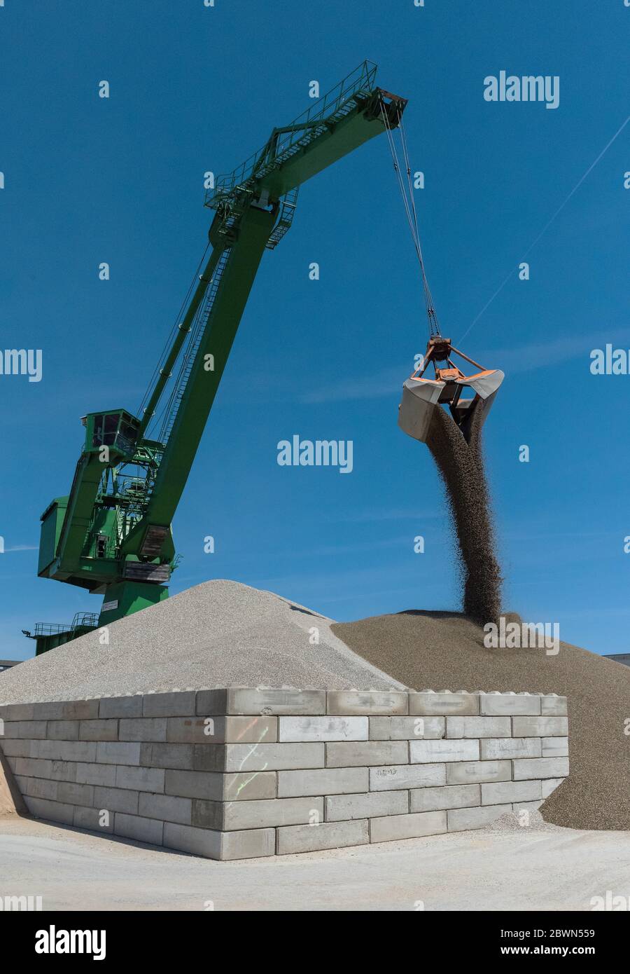 Green harbor crane pours sand and gravel onto a hill Stock Photo