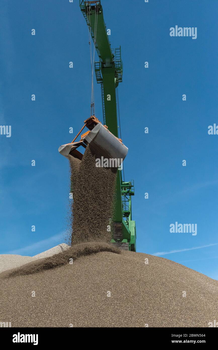 Green harbor crane pours sand and gravel onto a hill Stock Photo