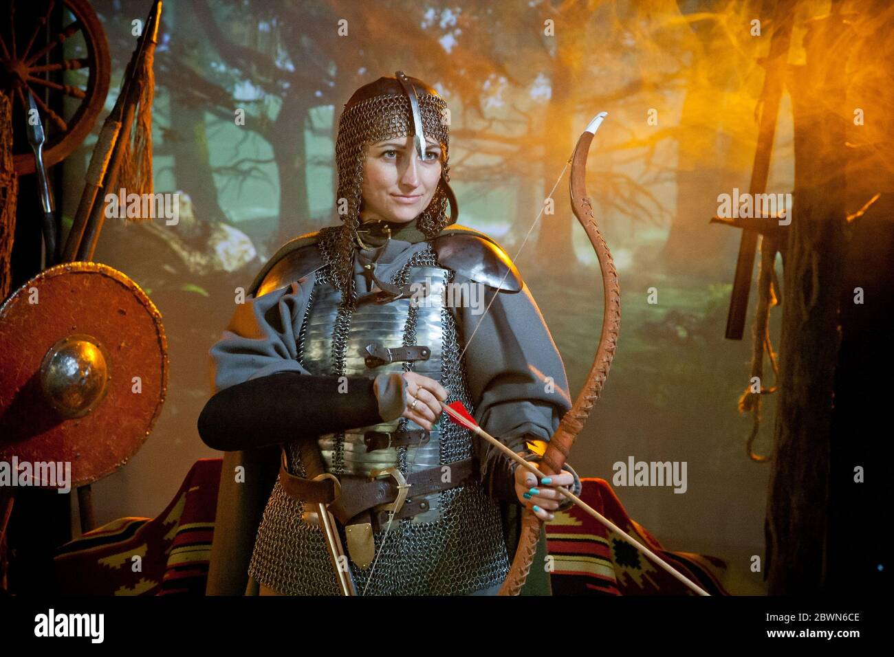 A smilingwoman in the costume of a warrior of the times of Kiev Rus in chain mail with a bow and arrows Stock Photo