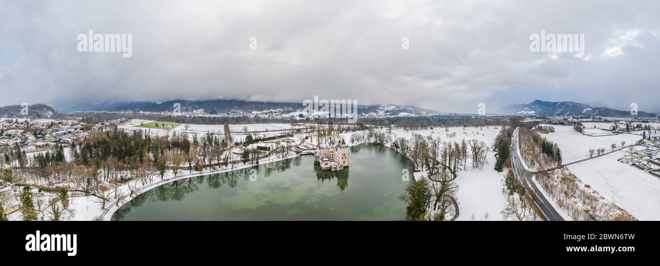 Panoramic aerial view of Schloss Anif moated castle in pond at Salzburg outskirts in heavy snow during winter with view of untersberg snow mountain Stock Photo