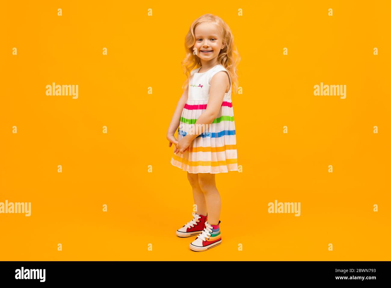blond girl in a bright striped summer dress in full growth on an orange background Stock Photo