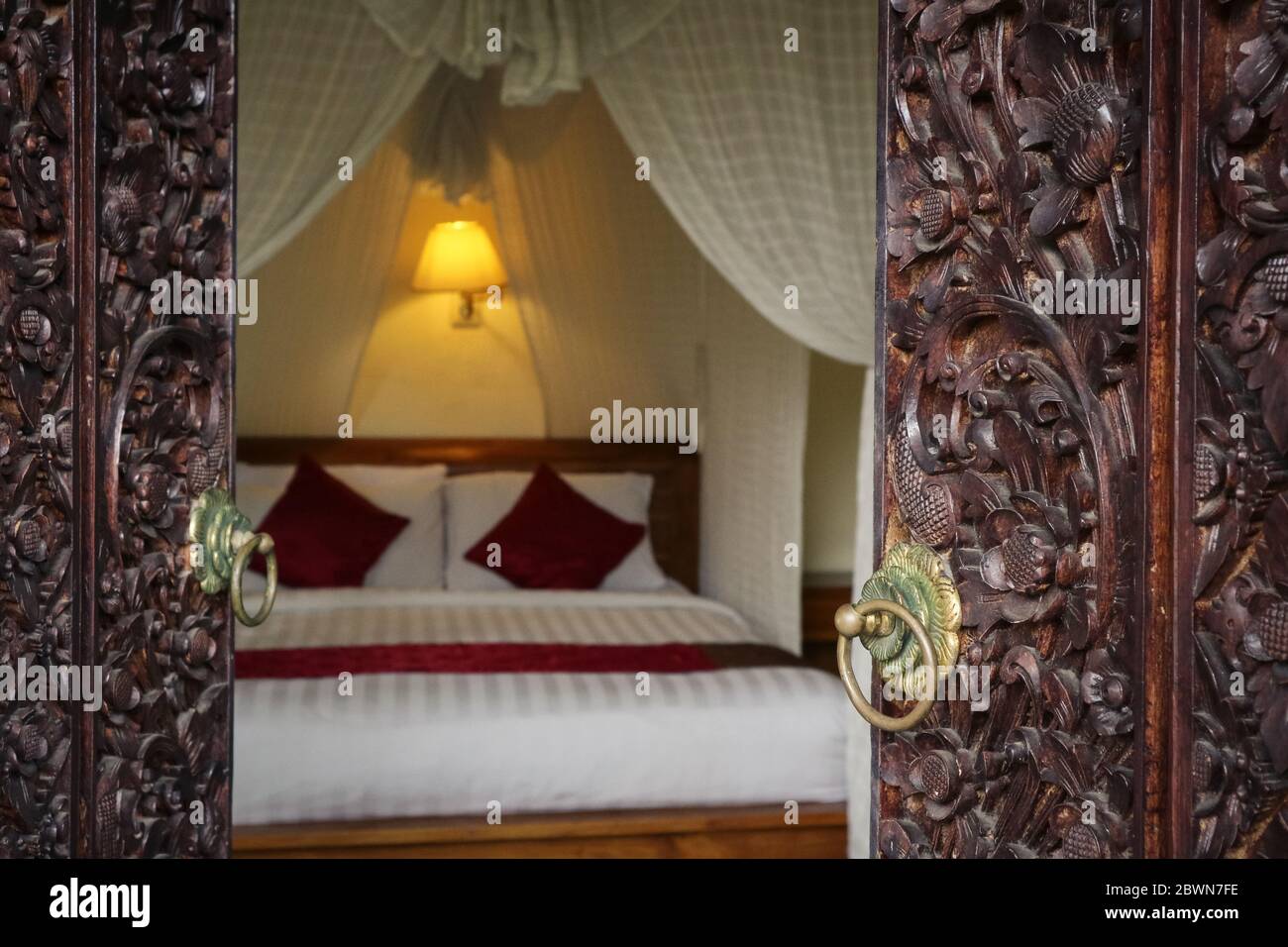 Traditional balinese bed with canopy. View through the opening of carved doors. Stock Photo