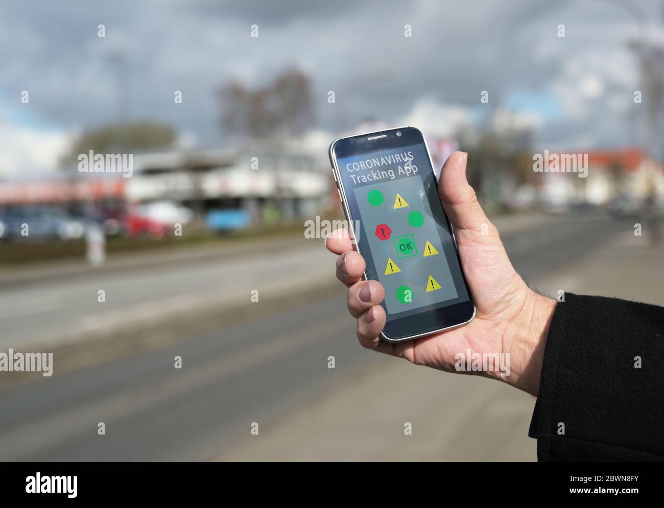 Hand is holding a smartphone with a coronavirus tracking app, which monitors contacts between people and shows the risk of infection, blurry city back Stock Photo