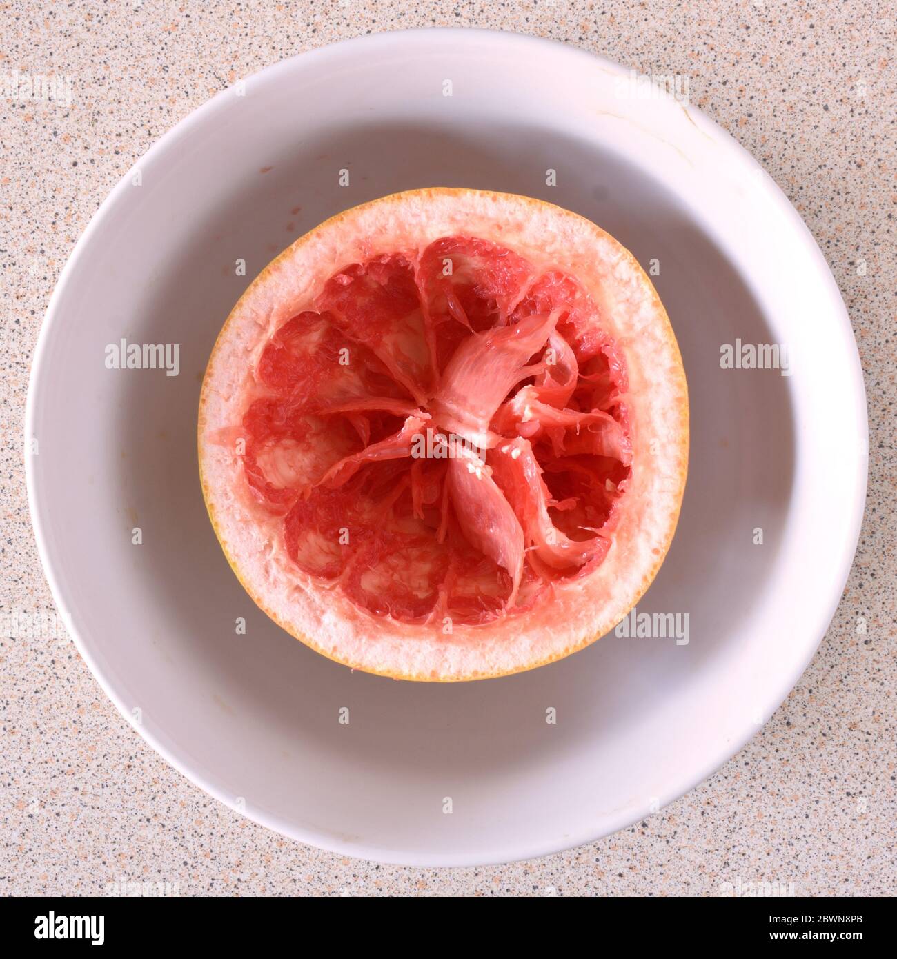 Aerial top down view of and eaten grapefruit in a white bowl on a light background Stock Photo