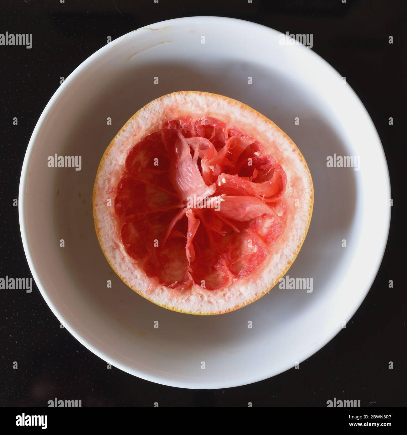 Aerial top down view of and eaten grapefruit in a white bowl on a black background Stock Photo