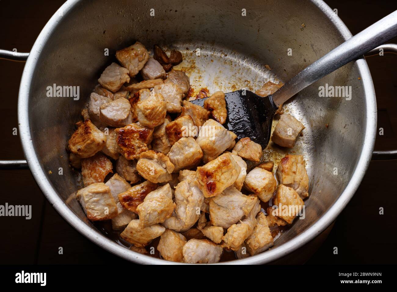Pieces of pork meat are seared in a stainless steel pot to get roasted aroma for a hearty stew, goulash or ragout, homemade cooking concept Stock Photo