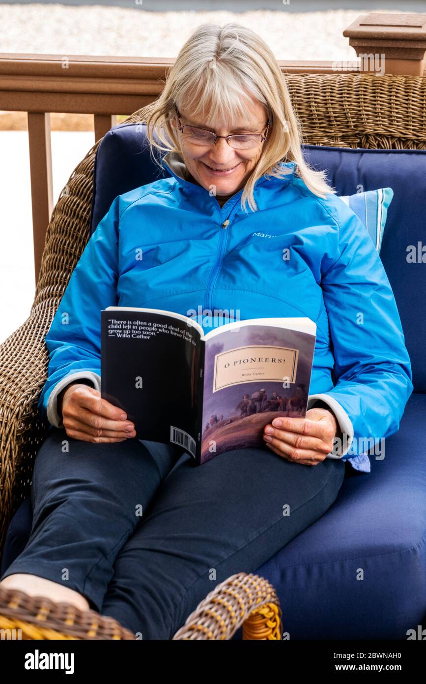 Senior woman reading a book on an outside residential patio Stock Photo ...