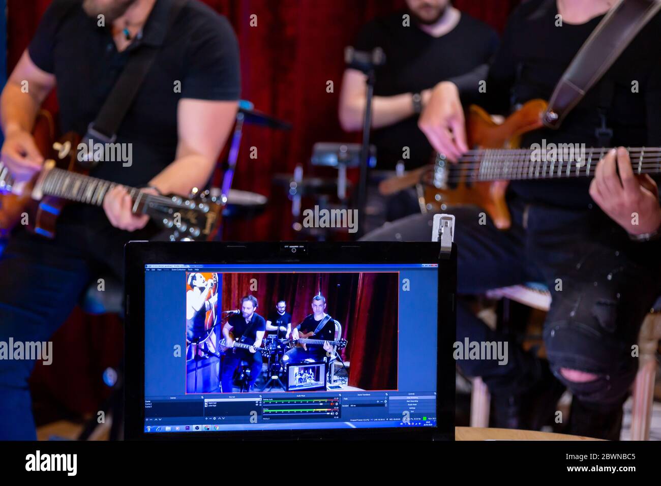 The band of Musicians Playing electric Guitar, Bass Guitar and Drums during the Concert broadcast Online on Social  Media Platforms in the Bar. Stock Photo