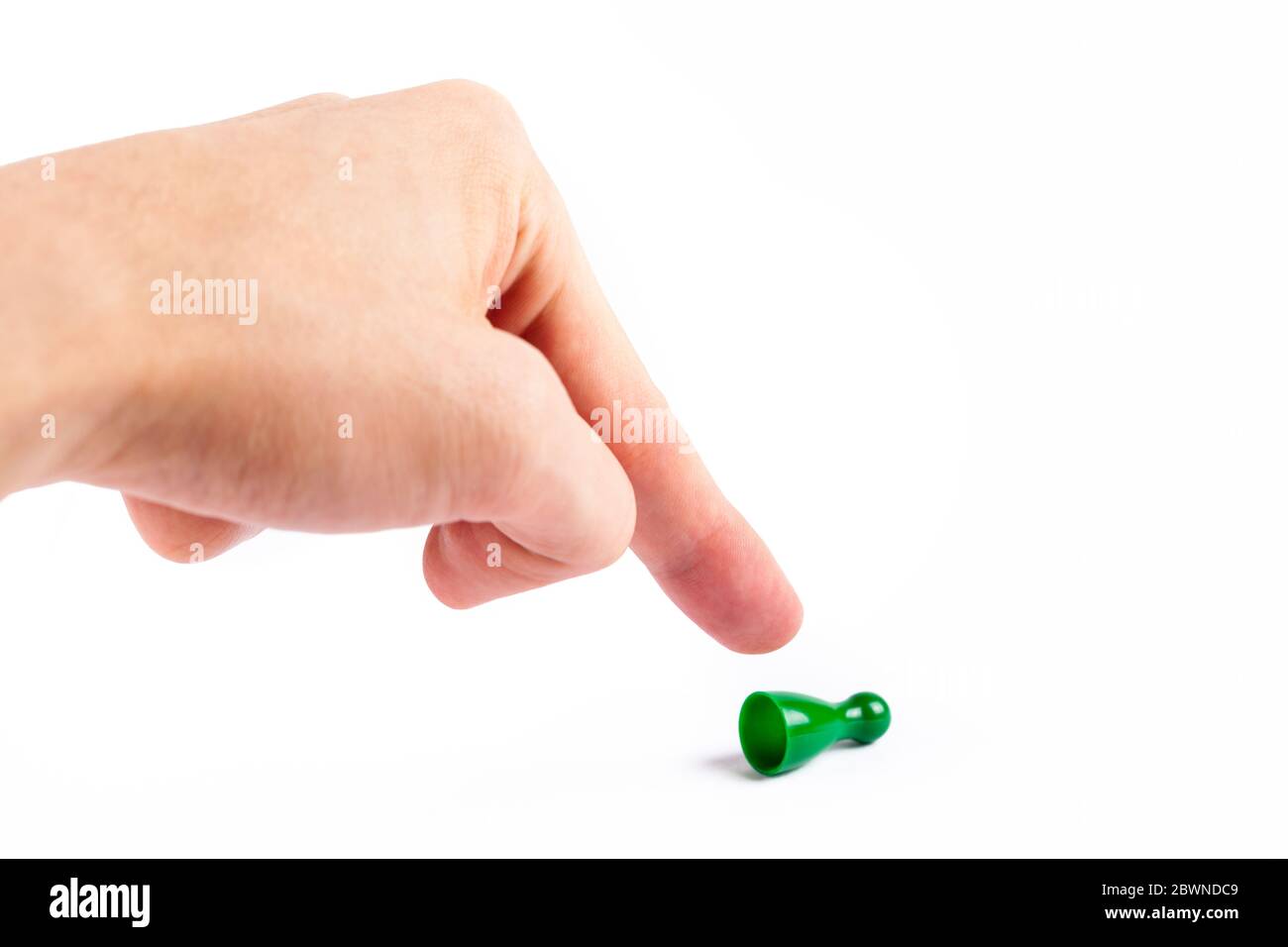 Human hand, finger flipping over a small game piece pawn pinning it down. Cornering, trapping someone, stay down gesture. Strong vs weak Stock Photo