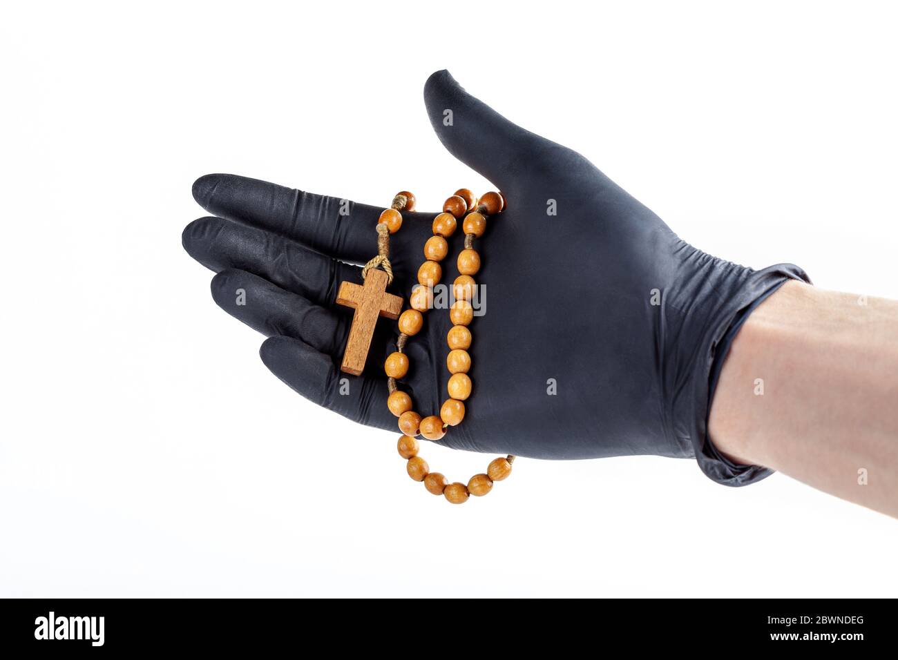 Hand in a black medical protective latex glove holding up a simple wooden christian rosary with a cross isolated on white, cut out. Safe prayer Stock Photo
