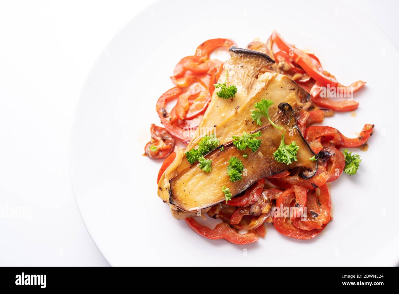 King oyster mushrooms on red bell pepper with parsley garnish served on a white plate, healthy vegetable meal for low carb diet and vegetarians, copy Stock Photo